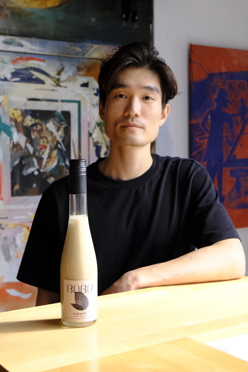 Tim standing behind the bar with a bottle of Babo Makgeolli on display.